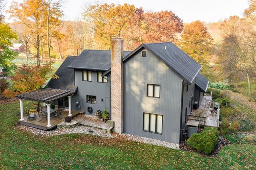 Aerial view of a gray home's rear pergola patio and brick chimney amid autumn woods