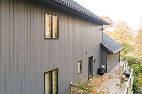 Close-up exterior of gray board-and-batten siding with tall windows and wood deck