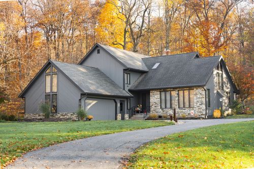 Gray farmhouse-style home with stone accents and curved driveway among fall foliage