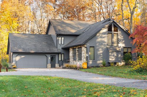 Two-story gray home with vaulted picture window and attached garage in an autumn setting