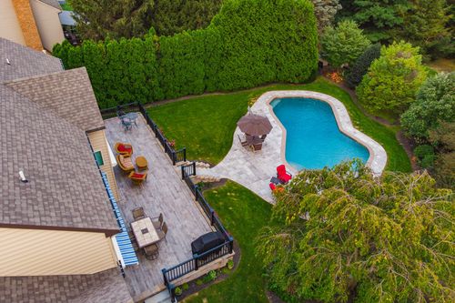 Aerial view of a backyard patio with lounge seating and umbrellas beside a curved pool