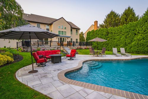 Backyard patio with red cushioned seating and umbrella overlooking a curved pool at dusk