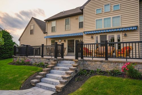 Home exterior with striped awnings, black deck railing and stone-edged staircase