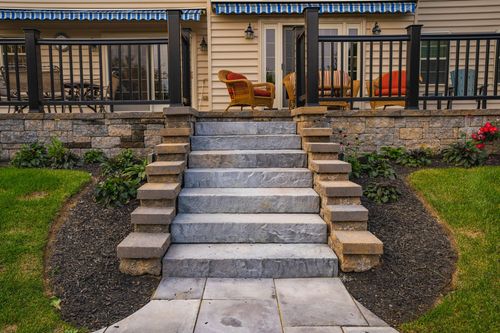 Stone staircase leading up to a covered deck with wicker patio chairs