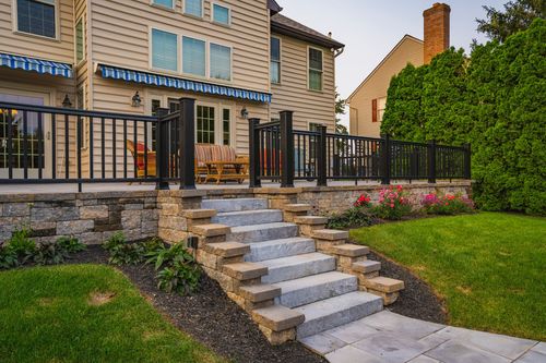 Home exterior with striped awning, deck seating and stone-edged staircase amid landscaping
