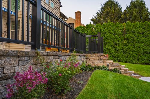 Side yard with black metal deck railing, stone retaining wall and flowering shrubs