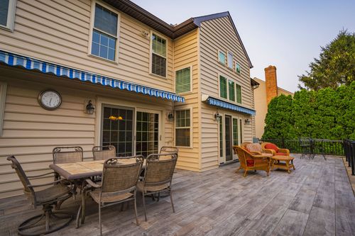 Wood deck patio with dining table, wicker seating and striped awnings on the home