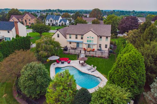 Aerial view of a large home with freeform pool, patio and umbrella seating at dusk