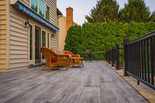 Composite deck with wicker lounge chairs, striped awning and tall hedge screening