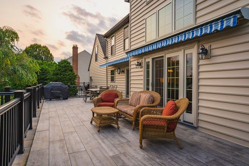 Covered deck with wicker seating, striped awning and grill overlooking the yard