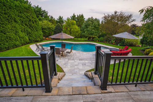 View through a black railing gate down stone steps to a freeform pool and patio