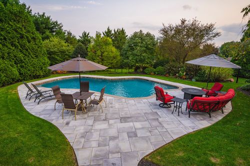 Backyard pool and stone patio with dining set, umbrellas and red lounge chairs