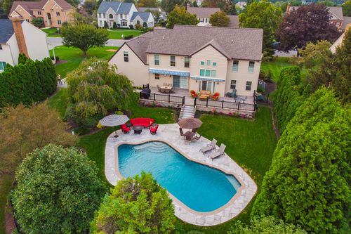 Aerial view of a stately home's backyard pool, patio furniture and deck with awning