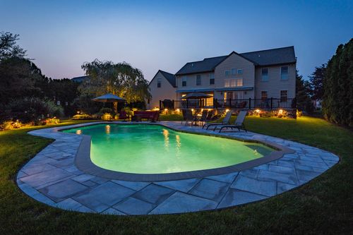 Home exterior at dusk with an illuminated green-lit pool and deck