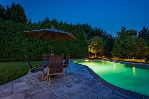 Patio seating with umbrella beside a glowing green pool at dusk