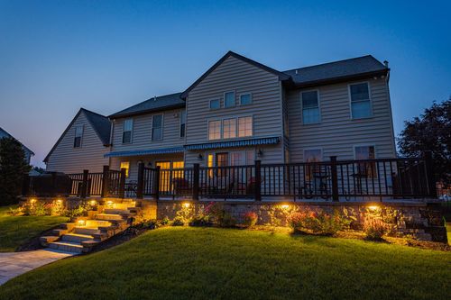 Home exterior at dusk with lit deck, awnings and landscape lighting on stone steps