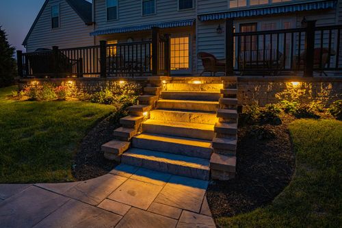 Illuminated stone steps and garden lighting leading to a home's deck at dusk