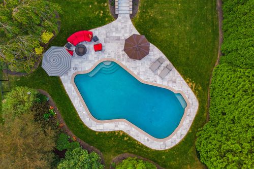 Aerial close-up of a freeform pool with stone patio, umbrellas and lounge chairs