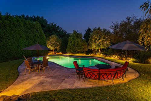 Backyard patio with red seating, umbrellas and a glowing pool lit at night