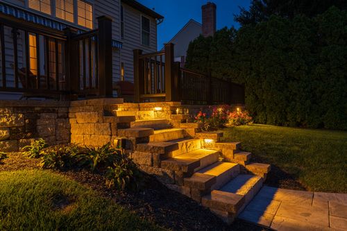 Illuminated stone steps leading up to a home's deck and stone retaining wall at night