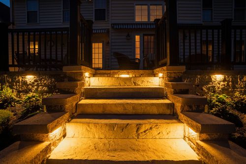 Illuminated stone staircase leading up to a covered home entrance at night