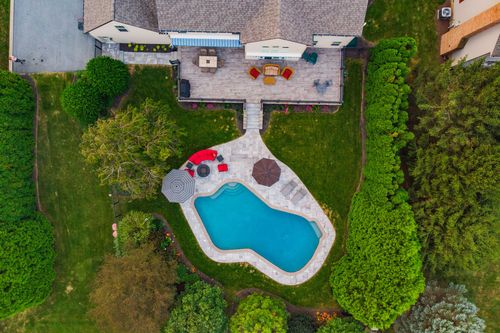 Aerial view of a home's rear deck, patio pool area and mature landscaping
