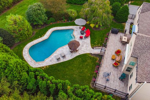 Aerial view of a gabled roofline beside a curved pool and stone patio at dusk