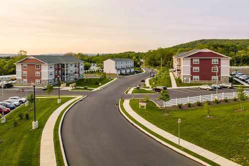Aerial view of an apartment complex entrance road with white fencing at sunset