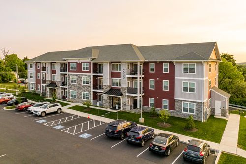 Aerial view of a red and gray apartment building with balconies and a full parking lot