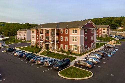 Aerial view of a red and tan apartment building with balcony units and full parking lot