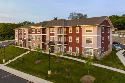 Aerial view of a red and tan apartment building with newly planted trees and stone base