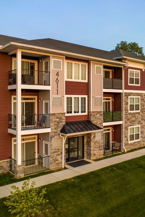 Close-up exterior of a red and tan apartment building with private balconies and stone entry
