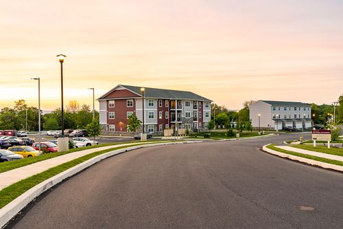Street view of an apartment complex driveway with buildings and parked cars at sunset