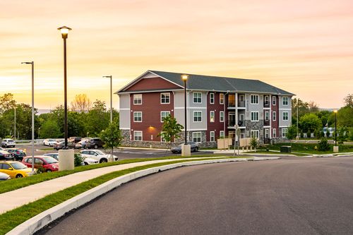 Apartment building exterior with lamppost lighting and a full parking lot at sunset
