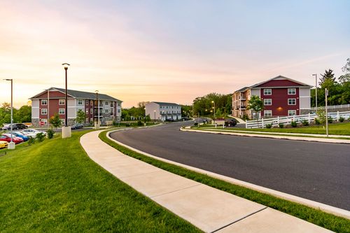 Street view of an apartment building and parking area with white fencing at sunset