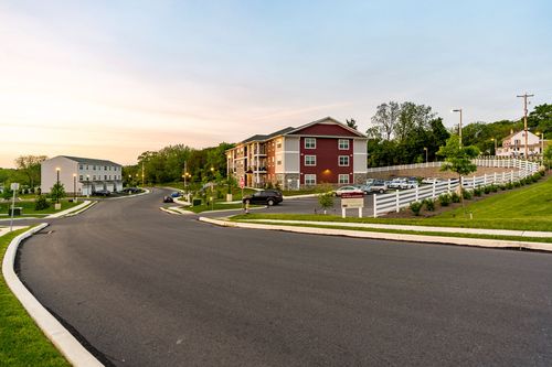 Street view of apartment buildings along a curved drive with white fencing at sunset