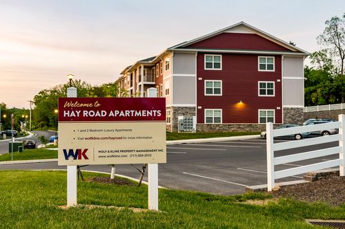Welcome sign for Hay Road Apartments in front of a red multi-family building at dusk