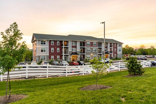 Multi-family apartment building with a young tree and cars parked along a white fence at sunset