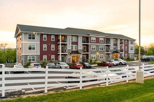Apartment building exterior with a stone base and glowing entrance behind a row of parked cars at twilight