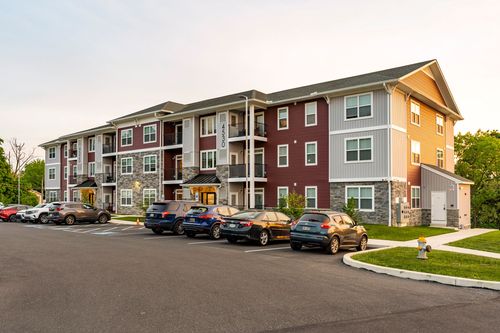Apartment building with tan, gray and stone siding overlooking a landscaped parking lot at dusk