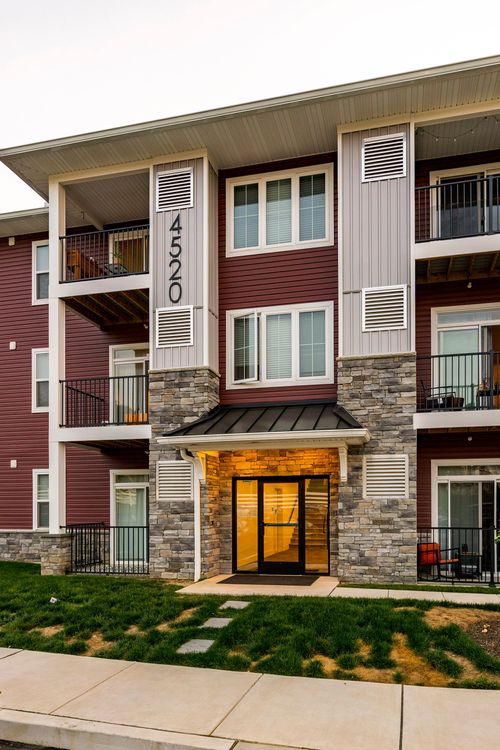 Close-up of an apartment building corner with a stone base, balconies and a black-roofed entry canopy at dusk