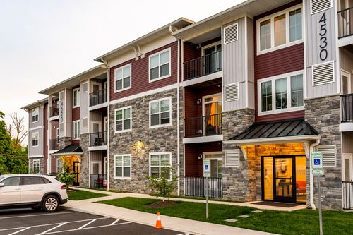 Apartment building facade with stacked balconies, stone accents and a lit entry canopy at twilight