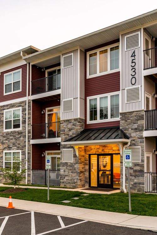 Apartment entrance with stone columns, accessible parking signage and a glowing glass door at dusk