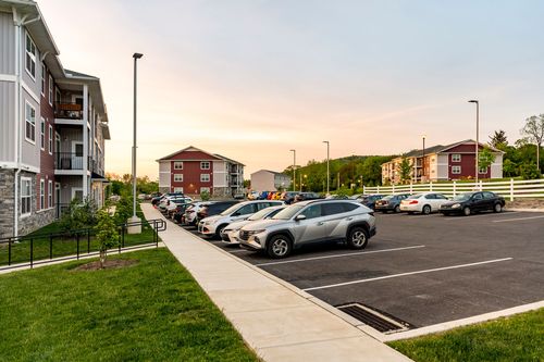 Apartment complex parking lot with cars lined along the curb and several buildings visible at dusk