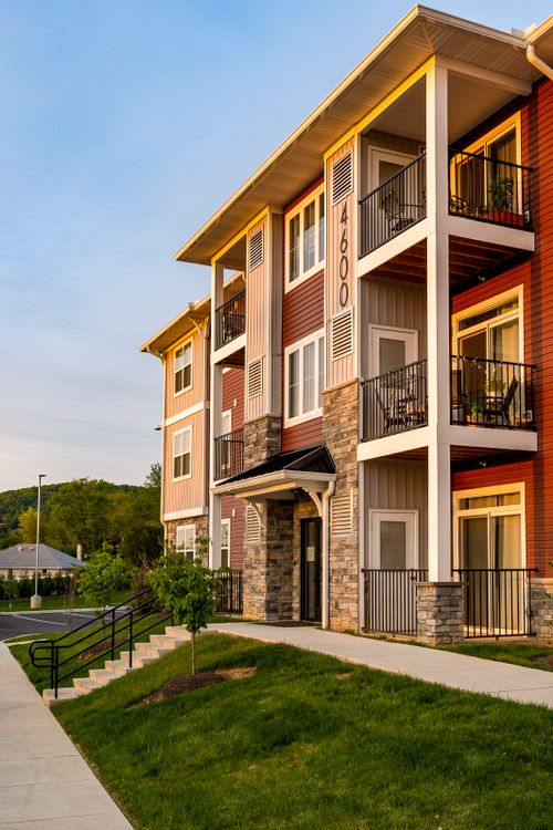 Apartment building with covered balconies furnished with chairs and a stairway up a landscaped hill at dusk