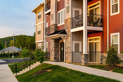 Apartment building corner with stacked balconies and a covered entry walkway lit at golden hour