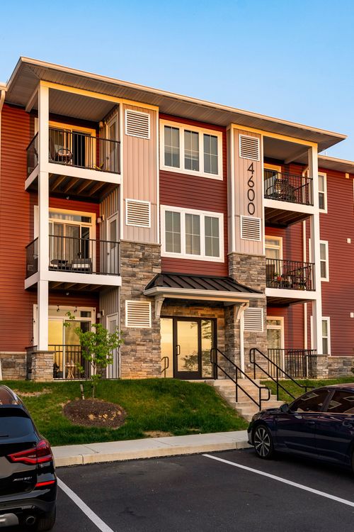Apartment building entrance with balconies above and a car parked out front under a clear sky