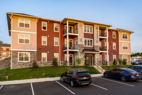 Apartment building exterior with an SUV and sedan parked in front and fresh landscaping at dusk