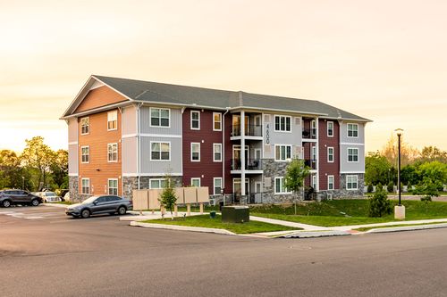 Apartment building with orange, tan and gray siding and a covered entry breezeway at dusk