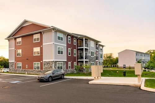 Apartment building with red and tan siding, a stone base and landscaped planting beds at sunset